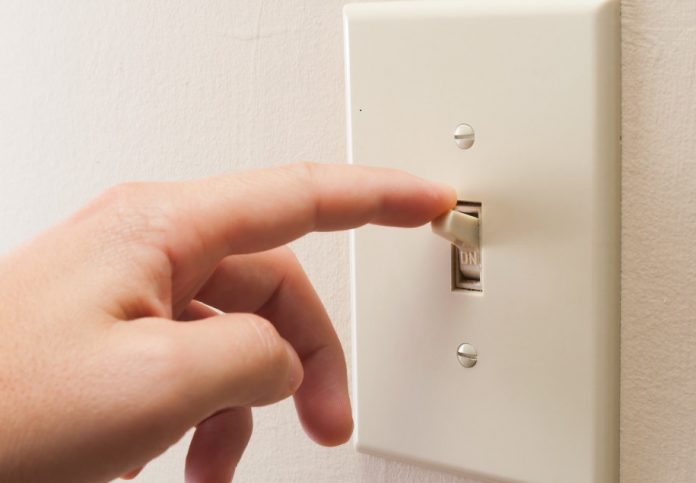 Hand turning wall light switch off. color image in horizontal orientation