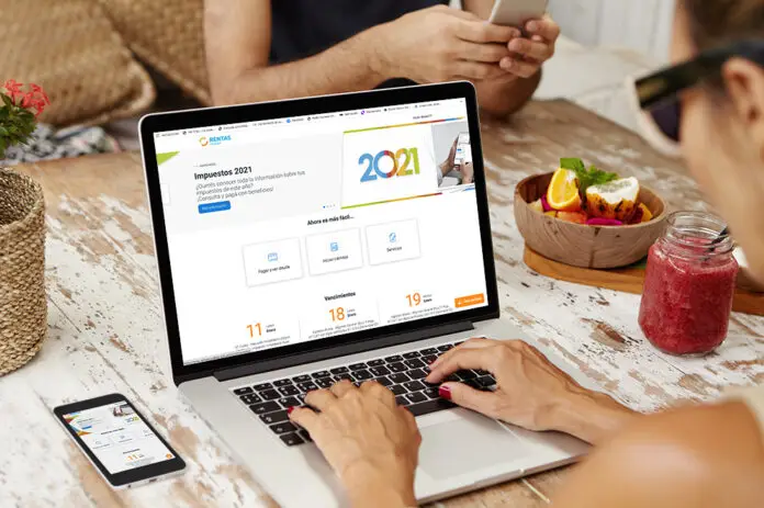 Caucasian woman in sunglasses surfing internet, viewing pictures and watching video via social media while having breakfast at cafe, sitting at wooden table with open laptop, cell phone and smoothie